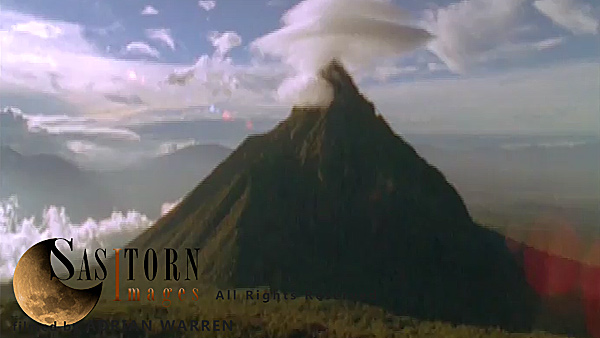 Forward tracking aerial shot, Virunga volcanoes, camera approaching Mt Mikeno with lenticular cloud on peak