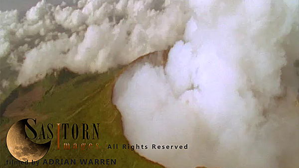 Forward tracking aerial shot, Virunga volcanoes, camera approaching smoking crater of Mt Nyiragongo surrounded by light broken of cloud in morning sun, camera tilts down over crater looking down through light broken cloud and tilts back up to horizon