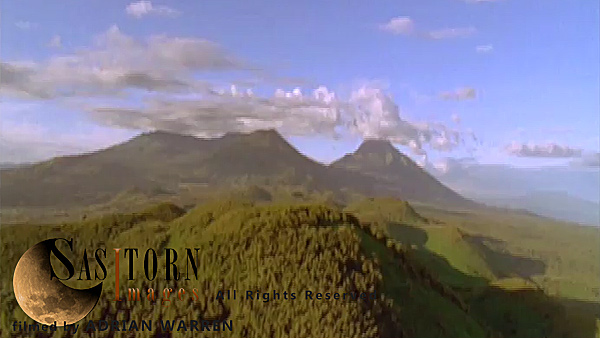 Forward tracking aerial shot, Virunga volcanoes, camera passes low over cratered forest between Sabyinyo and Visoke (Bisoke) in morning sun, Visoke (Bisoke) and cloud topped Mikeno and Karisimbi in background, camera tilts down and turns into sunlight in front of Visoke (Bisoke)
