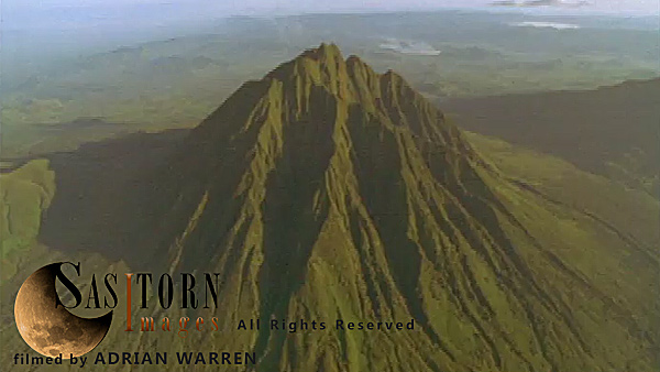 Forward tracking aerial shot, Virunga volcanoes. camera passing high over Mt Sabyinyo in morning sun, camera tilts down slowly as knife edge ridges fill shot, camera passes over summit tilting down over ridges with small wisps of cloud