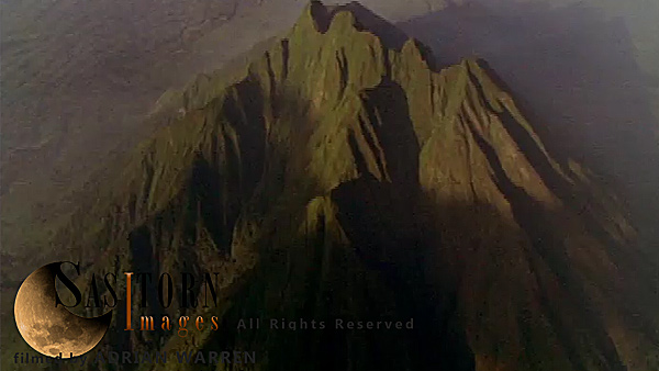 Forward tracking aerial shot, Virunga volcanoes, camera approaches Mt Sabyinyo in morning sunlight with Karisimbi, Visoke (Bisoke) and Mikeno in background, camera slowly tilts down to show detail of summit